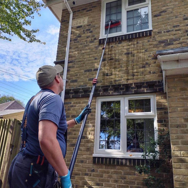 A person using a pole to clean a window on a two-storey house.